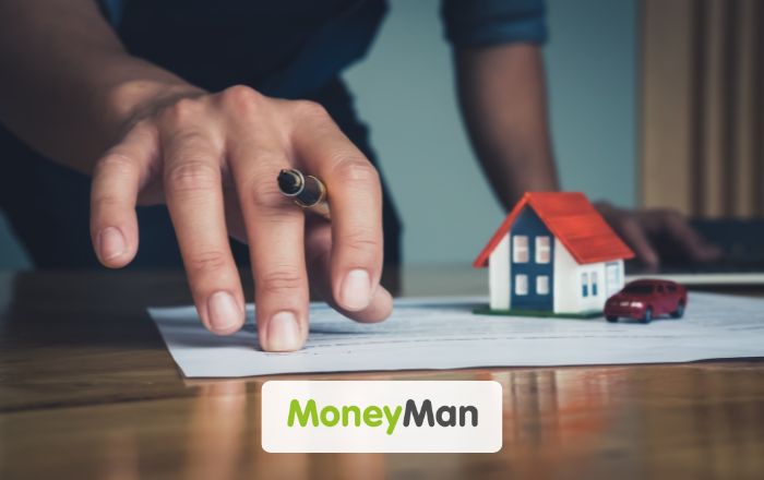 imagem com a mão de um homem segurando uma caneta e arrastando um papel sobre uma mesa. Na parte de baixo está o logo da moneyman
