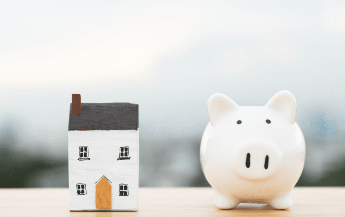 portabilidade de financiamento imobiliário - imagem com uma casa de papel em cima da mesa e ao lado da casa um cofrinho de porco.
