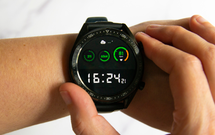 Relógio inteligente exibindo dados de saúde e hora, incluindo batimentos cardíacos, passos diários, clima e horário, usado no pulso de uma pessoa.